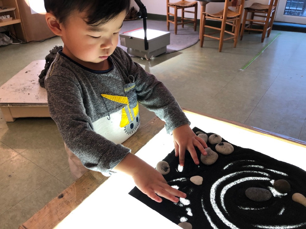 child running fingers through black sand