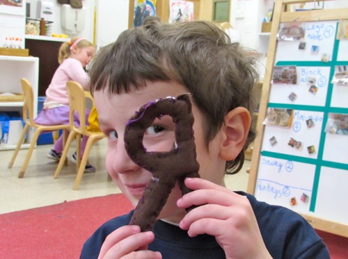 Child looking through a stuffed cushion shaped as the letter r