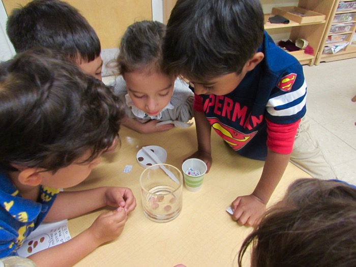Children looking at a glass of coins in water