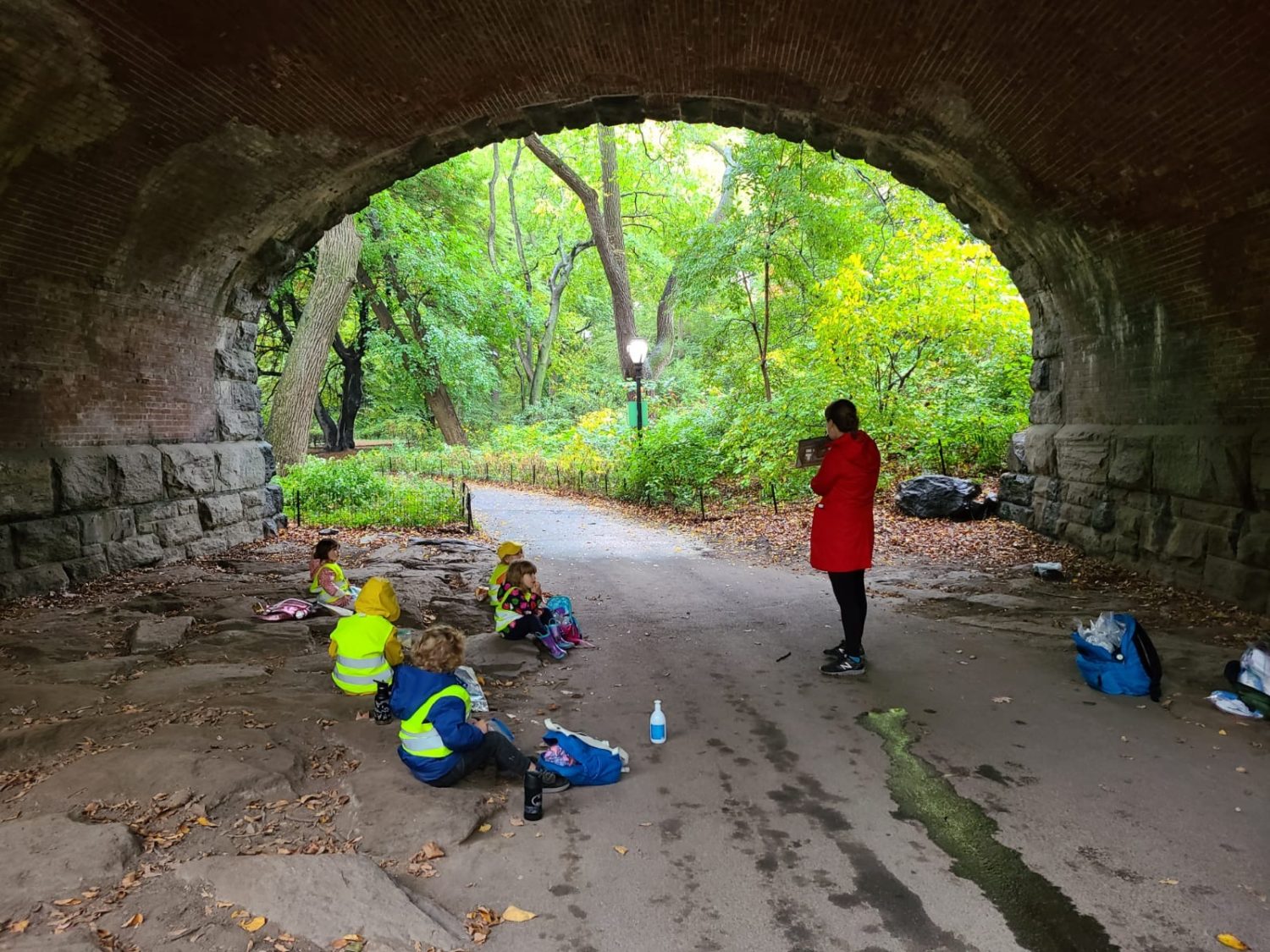 a teacher reading a book to kids under a bridge in park